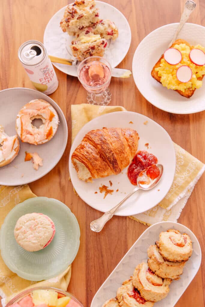 Image of brunch foods including toast with egg, bagel with lox, and scones, accompanied by a Frenchie cocktail mimosa.